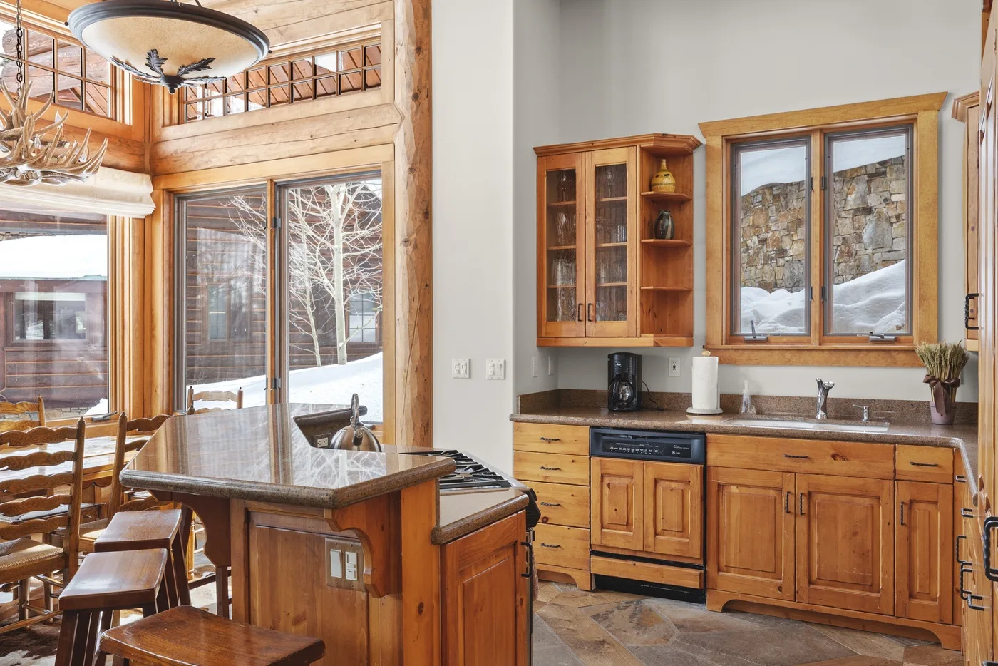 A wood-paneled kitchen and dining area with a central island and snowy views through the windows.