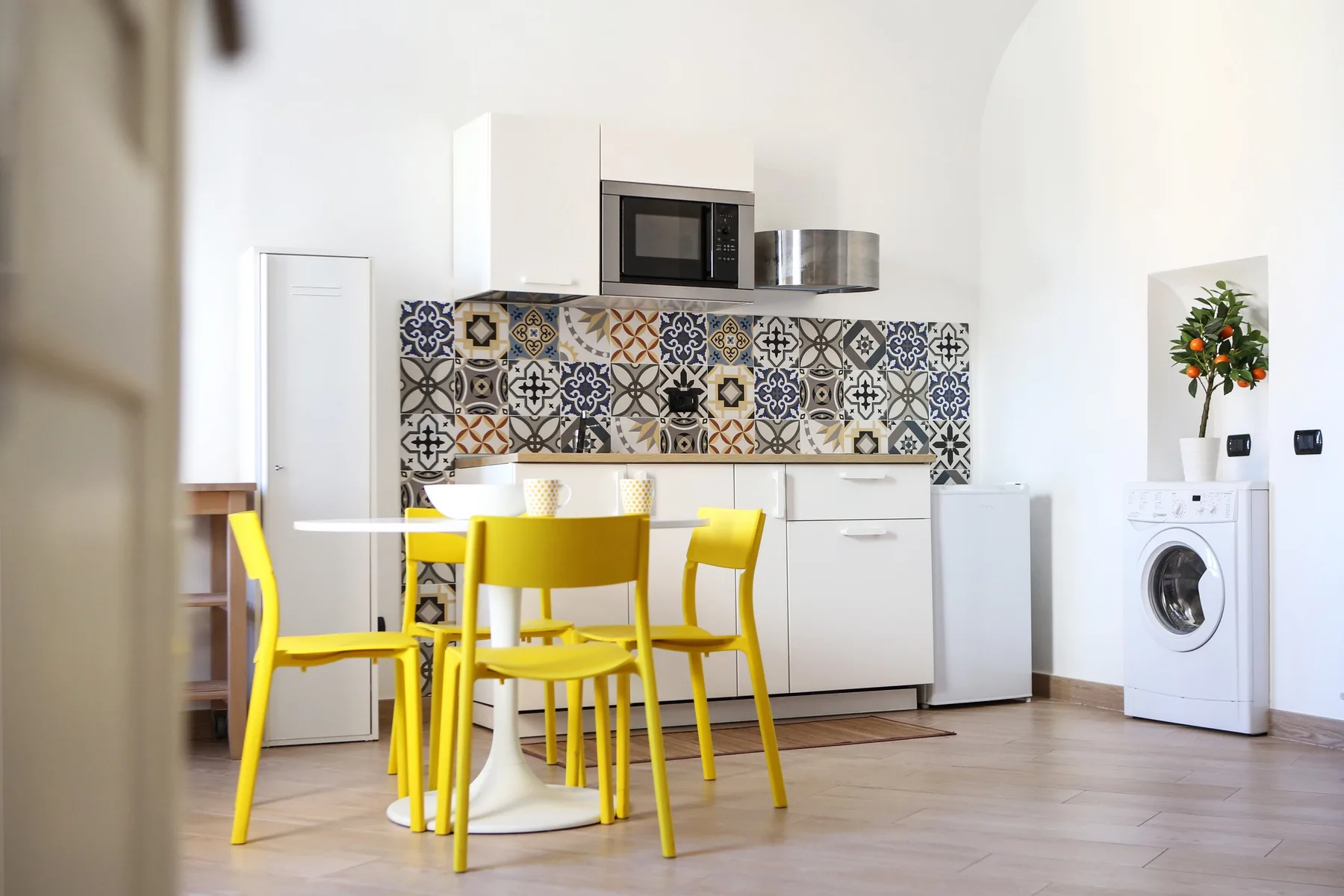 A bright kitchen with yellow dining chairs and a patterned backsplash.