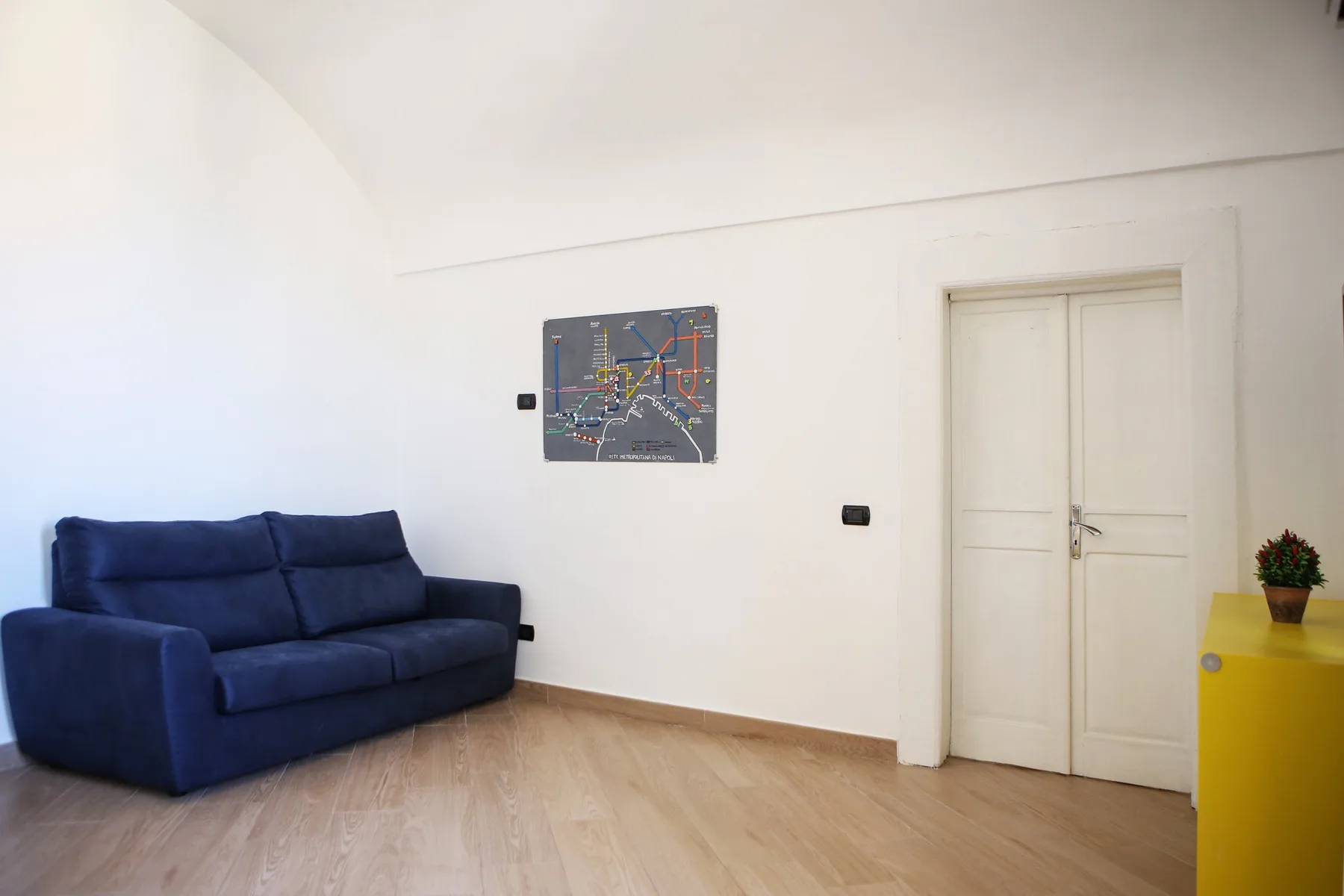 Una sala de estar con un sofá azul, arte en la pared y suelo de madera clara.