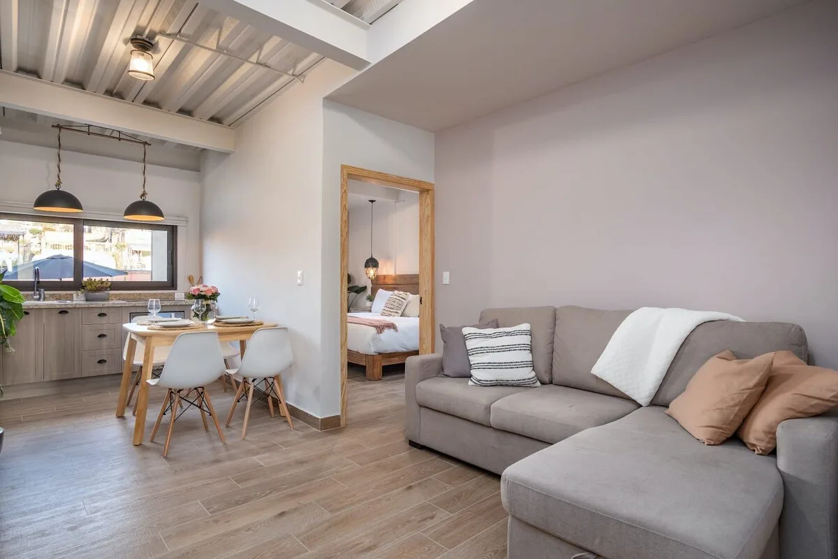 An open-plan living room and kitchen with a gray sectional and dining table.