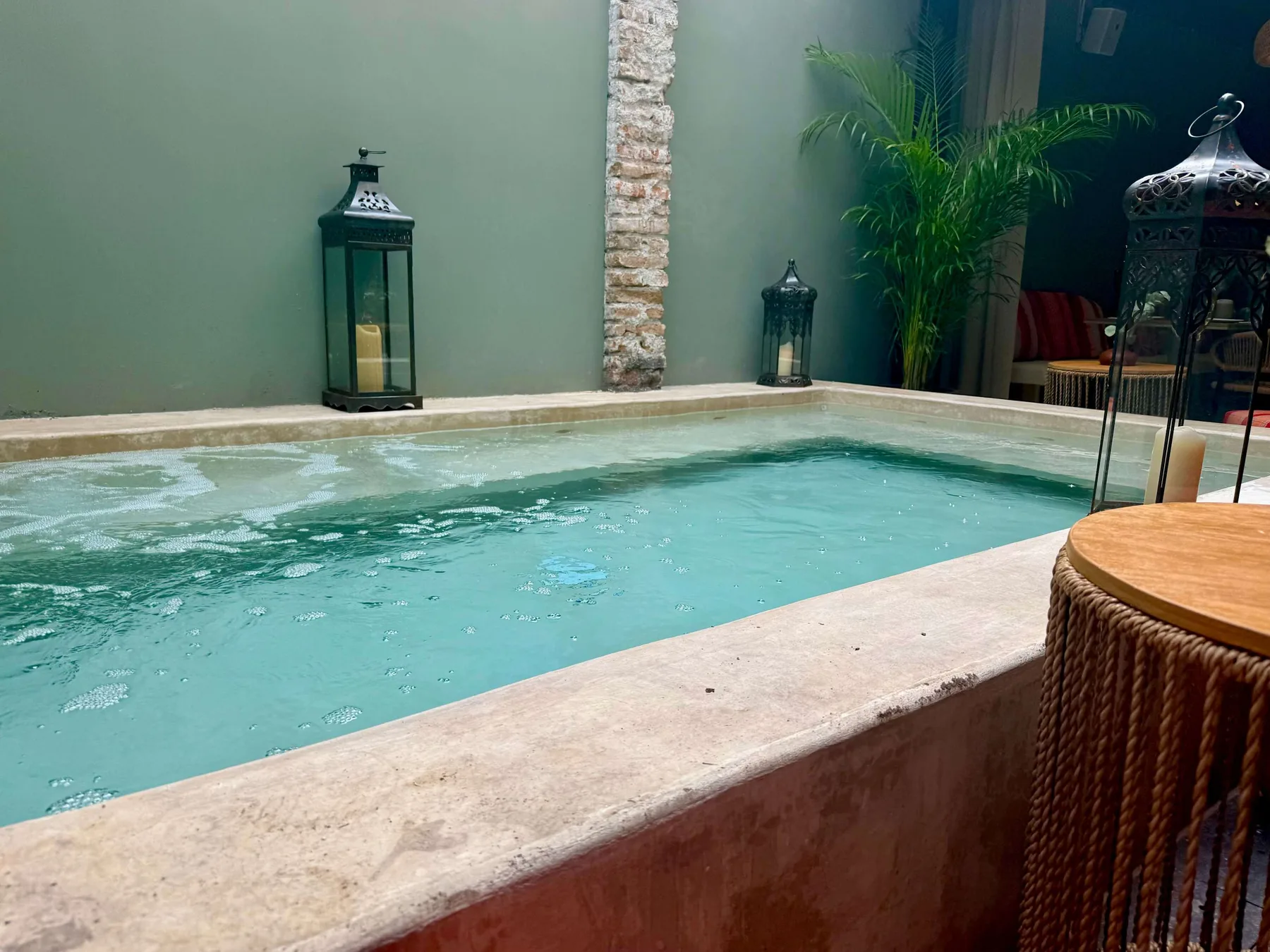 An indoor pool with lanterns and a potted palm beside the water.