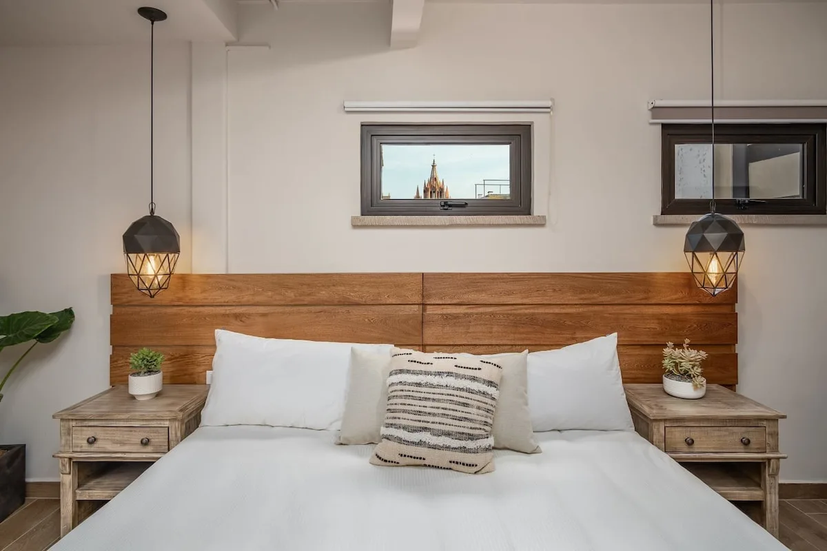 A bedroom with a bed beneath a wooden headboard and two small windows.