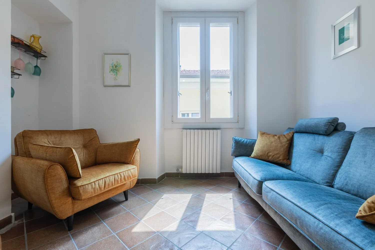 Una sala de estar con asientos marrones y azules junto a una ventana luminosa.