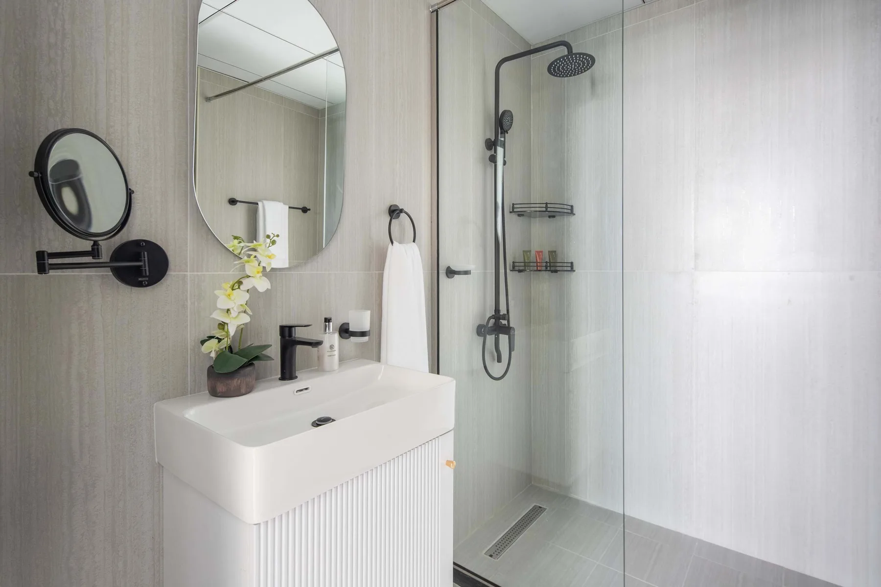 Un lavabo con espejo está junto a una ducha con mampara de vidrio.