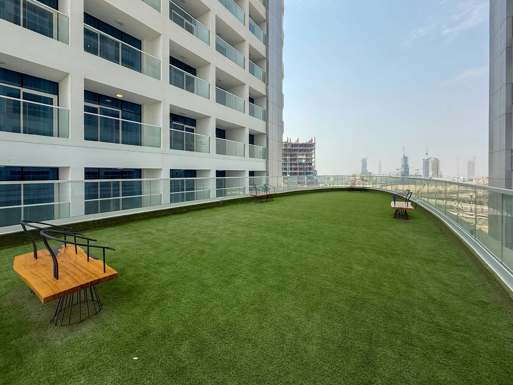 Una terraza en la azotea con césped artificial, asientos y barandillas de vidrio con vistas a la ciudad.