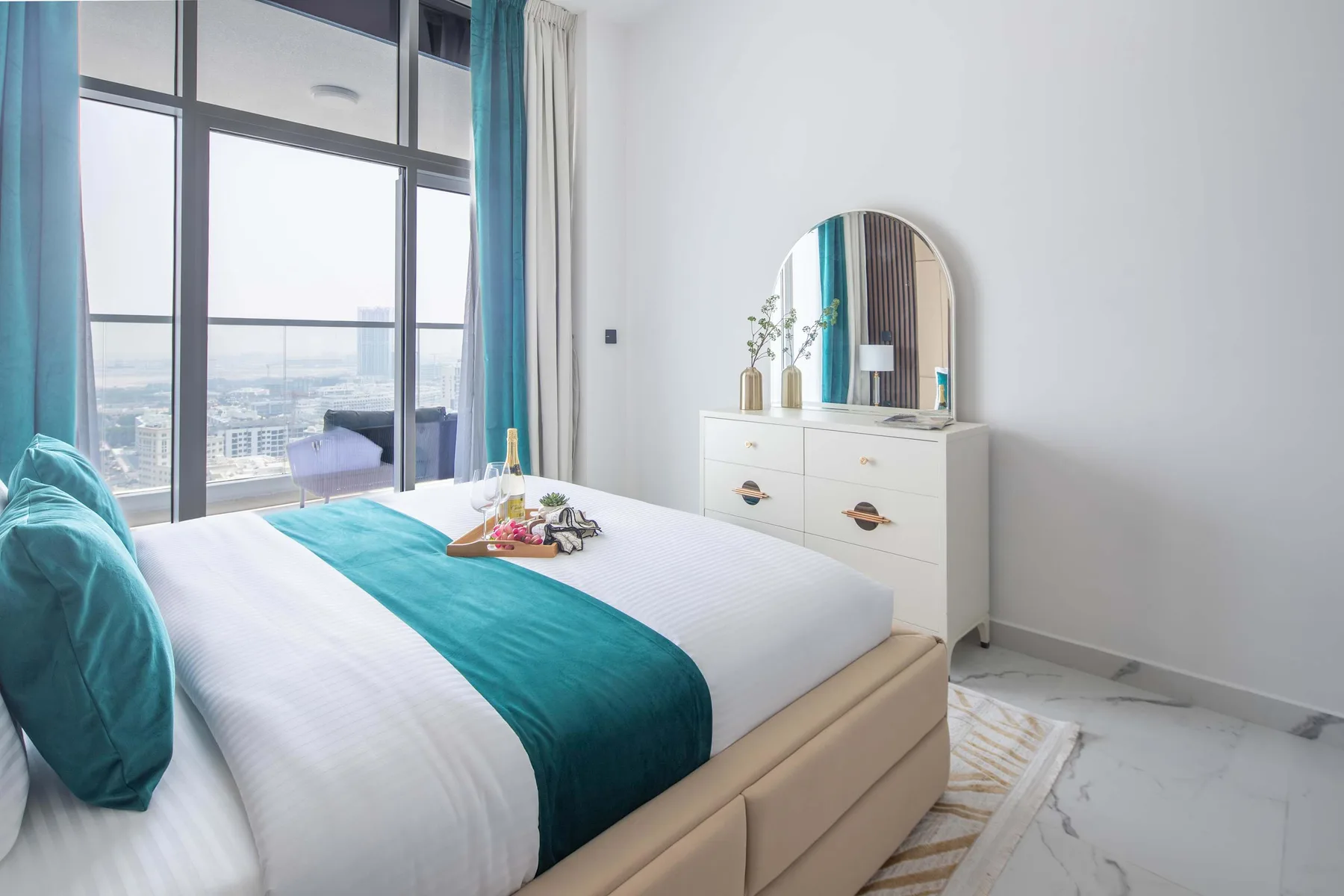 Un dormitorio luminoso con una cama junto a grandes ventanas y una cómoda.