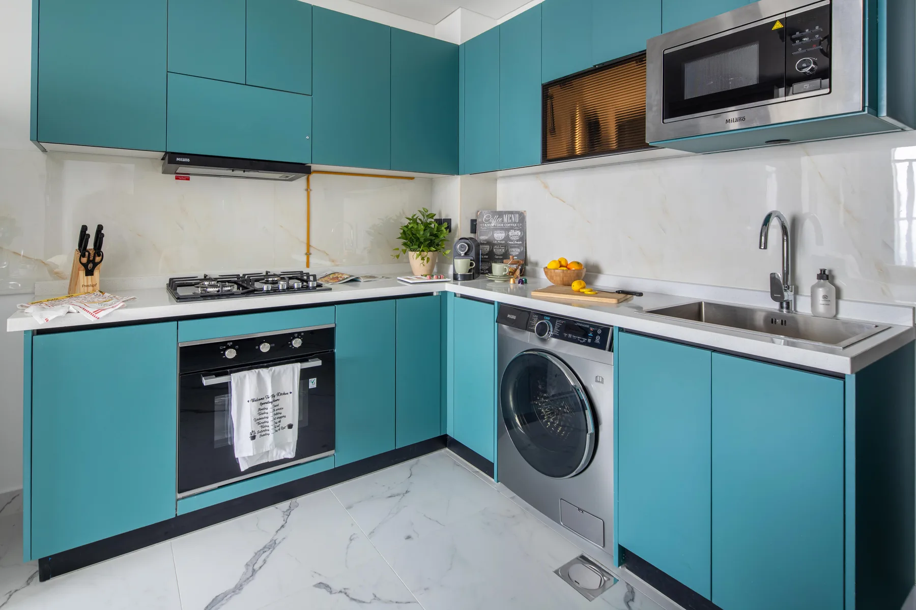 Una cocina moderna con gabinetes verde azulado, una placa de cocina, horno y fregadero.