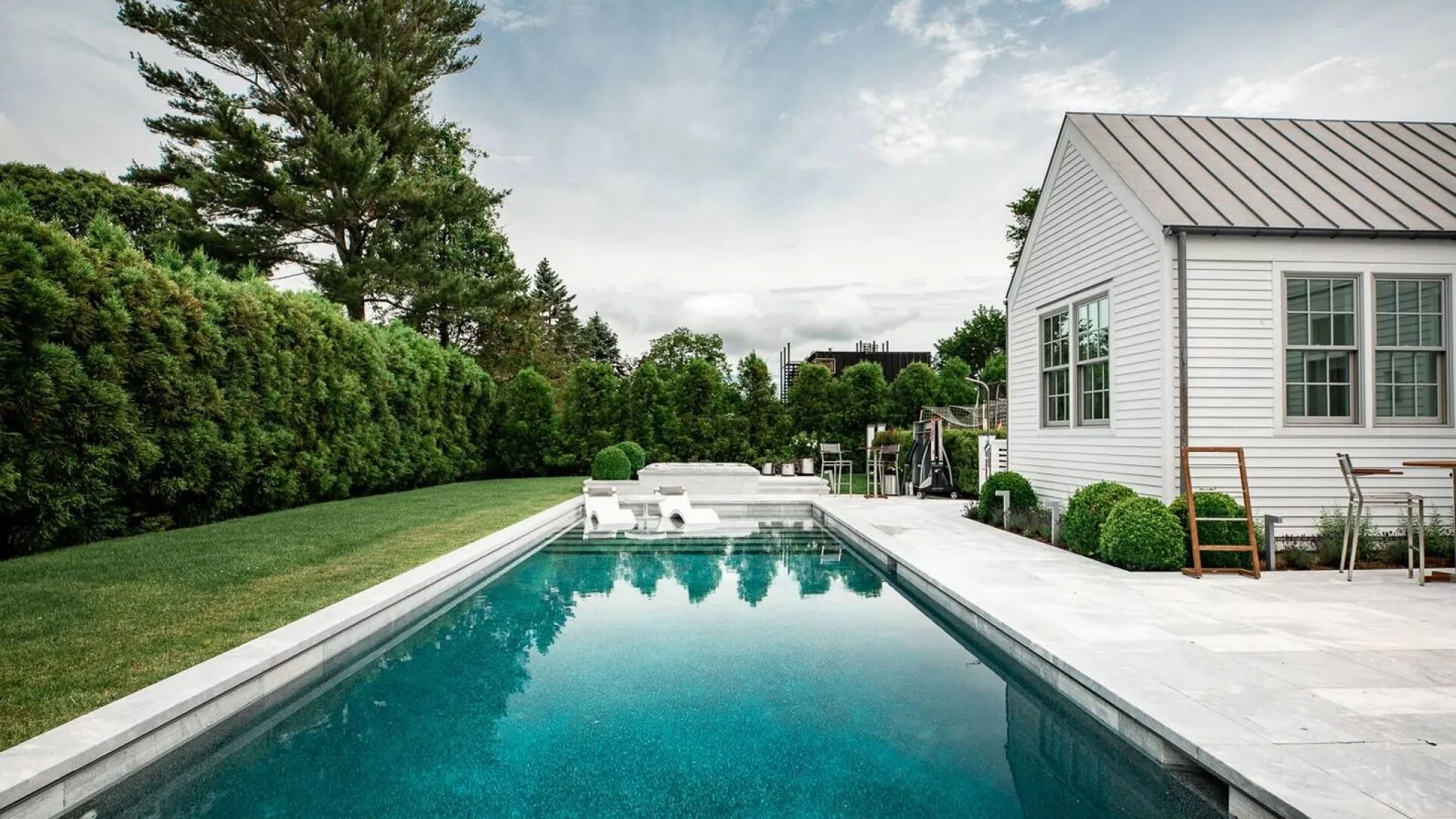 Una piscina al aire libre junto a una casa blanca y un jardín cuidado.