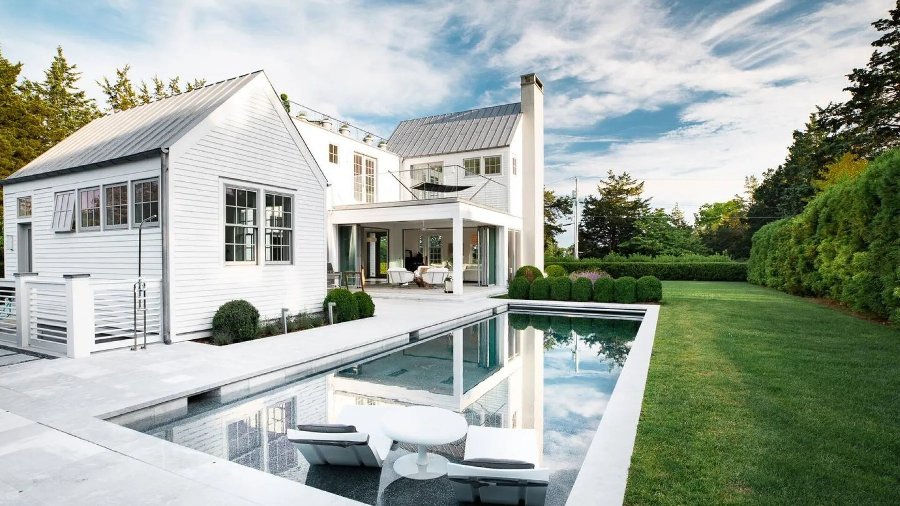 Una casa blanca moderna da a una piscina rectangular y un césped.