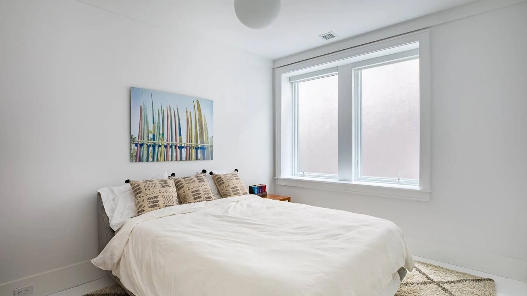 Un dormitorio luminoso con una cama bajo una ventana amplia.