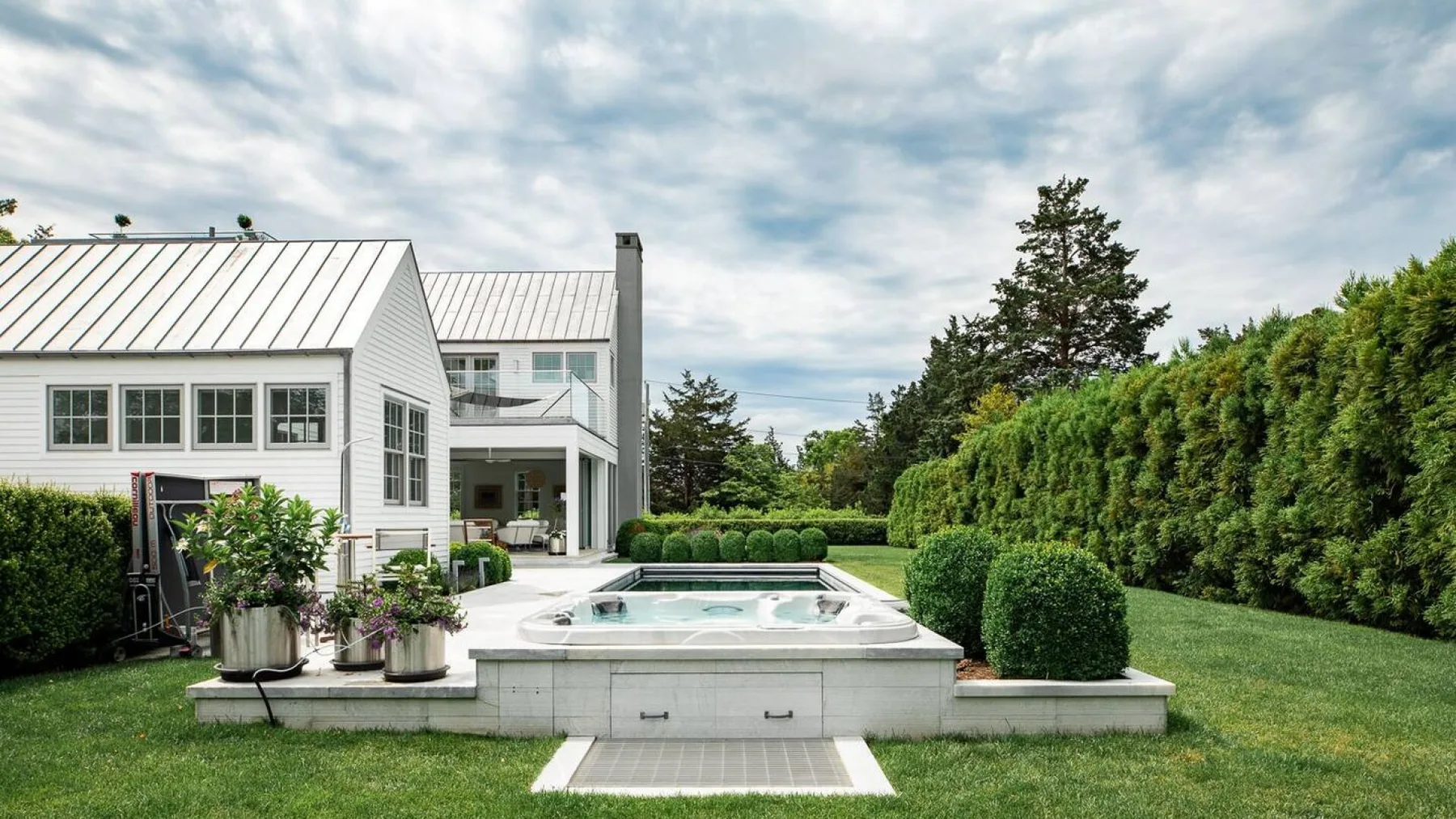 Un jardín ajardinado con una piscina elevada al aire libre junto a una casa blanca.