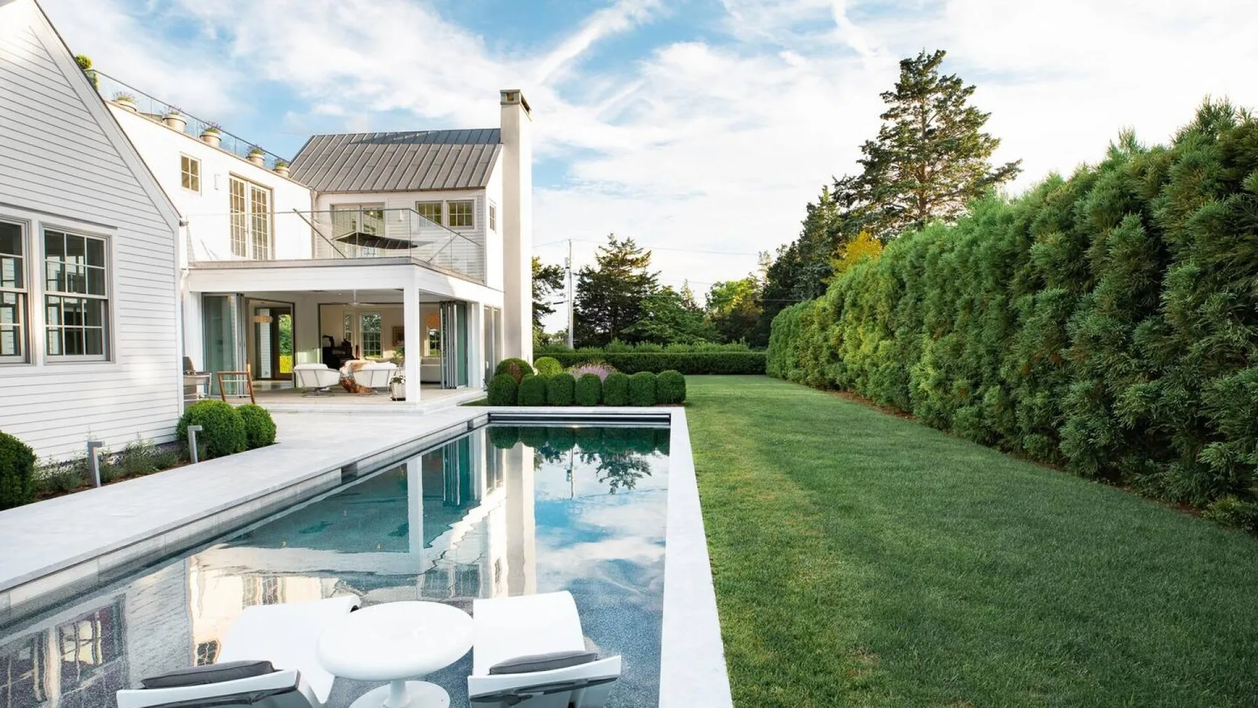 Una casa blanca da a una piscina exterior alargada junto a un césped verde.