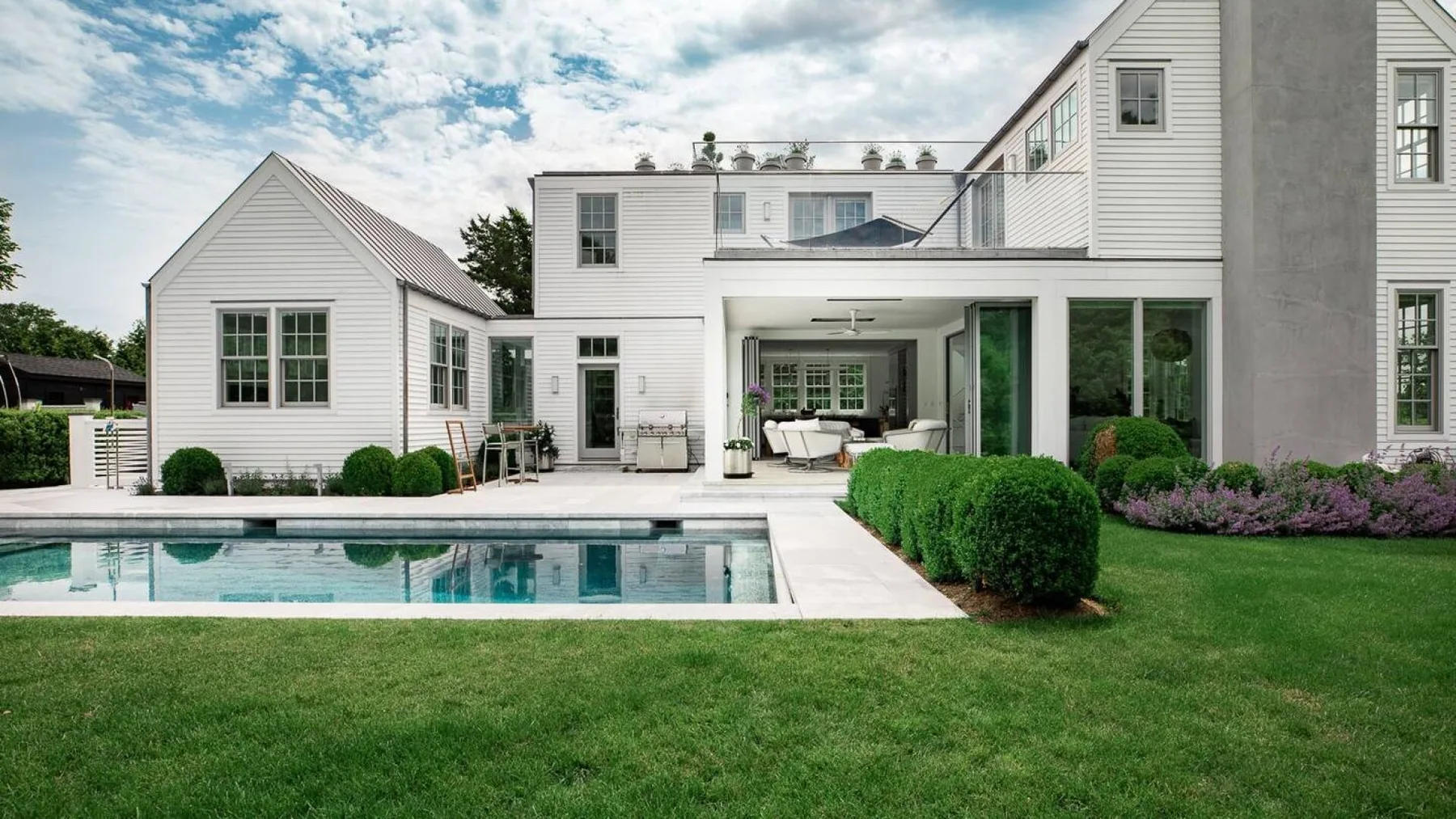 Una casa blanca da a una piscina y un césped verde.