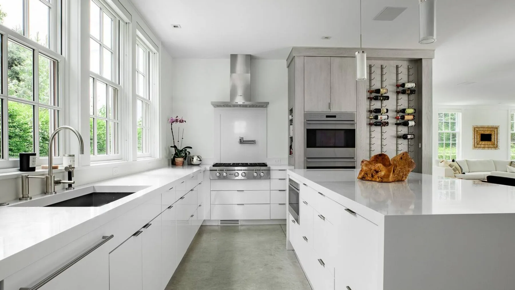 Una cocina moderna y luminosa con encimeras blancas y grandes ventanas.