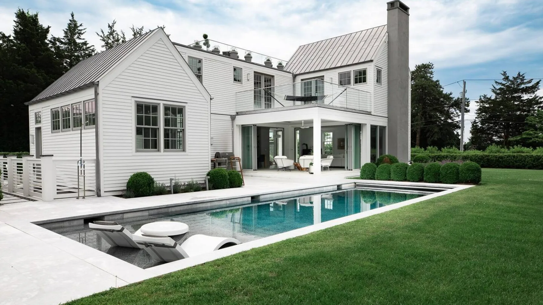 Una casa blanca se encuentra junto a una piscina rectangular y un césped.