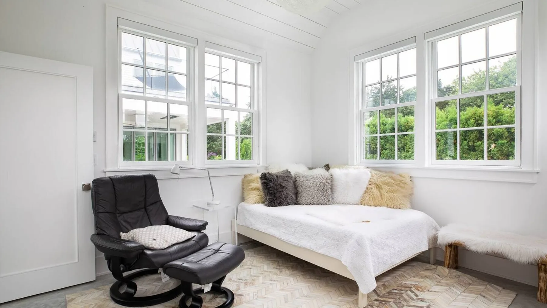 Un dormitorio luminoso con una cama blanca y grandes ventanas que dan a la vegetación.