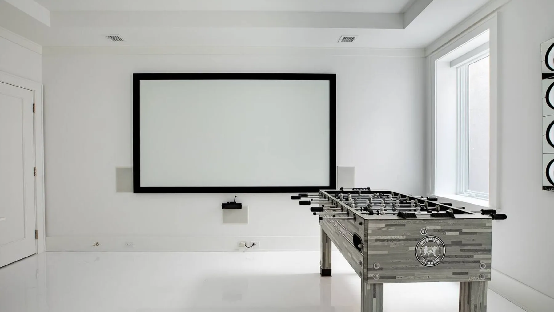 Una luminosa sala de recreación tiene un futbolín y una gran pantalla en la pared.