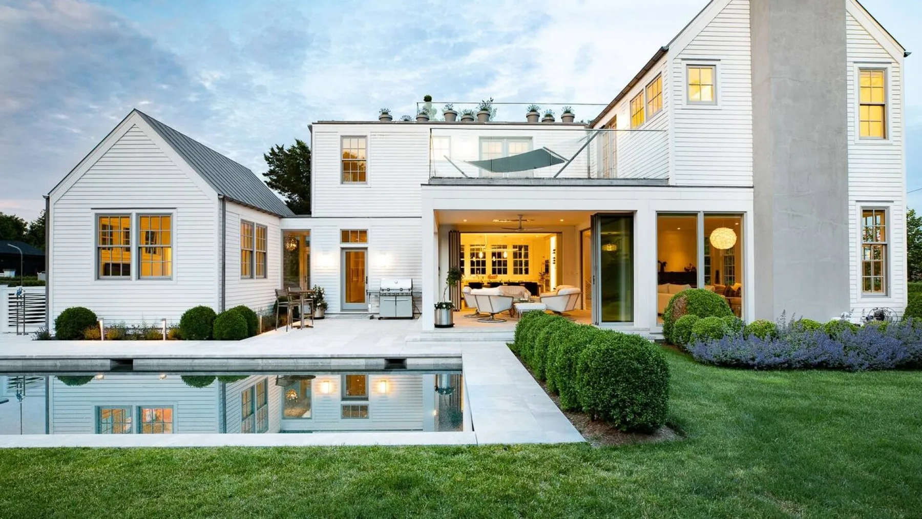 Una casa blanca moderna da a una piscina reflectante y un césped ajardinado.