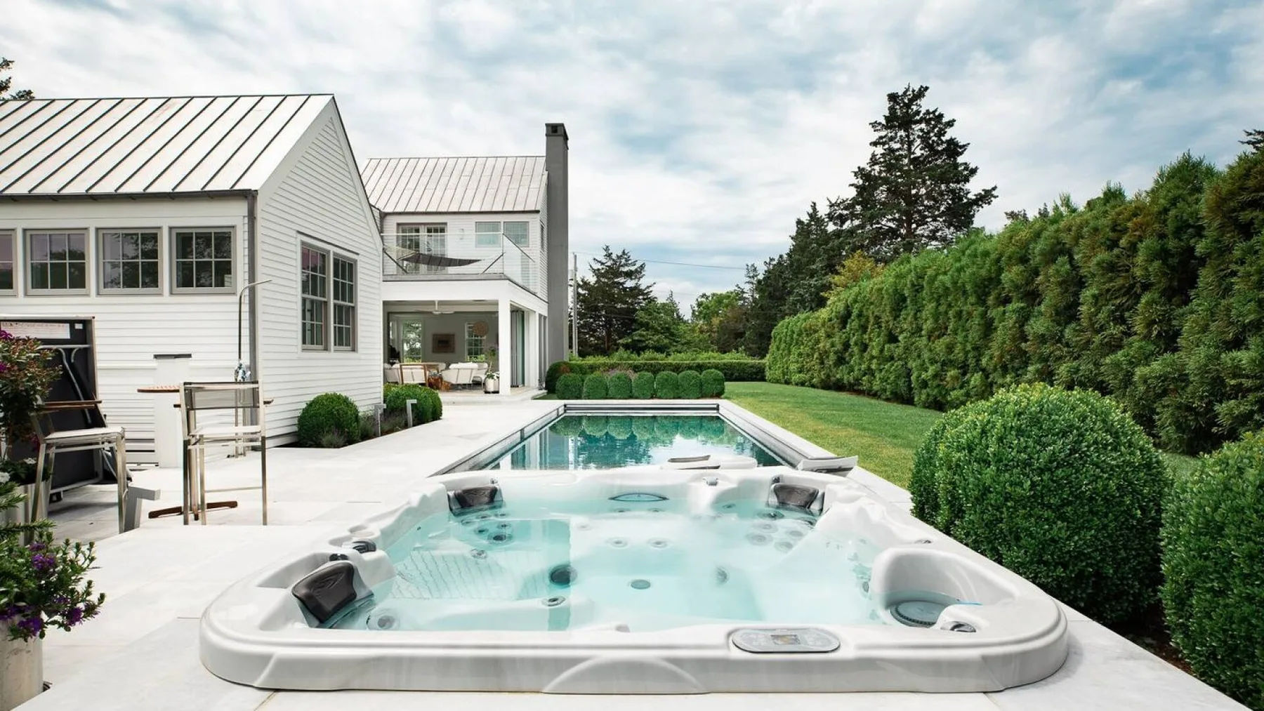 Un patio trasero con un gran spa empotrado junto a una casa blanca.