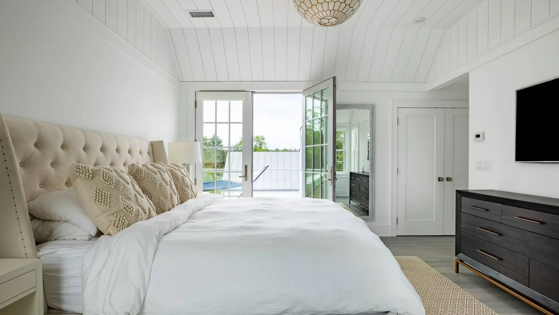 Un dormitorio luminoso con una cama blanca y puertas de vidrio abiertas.