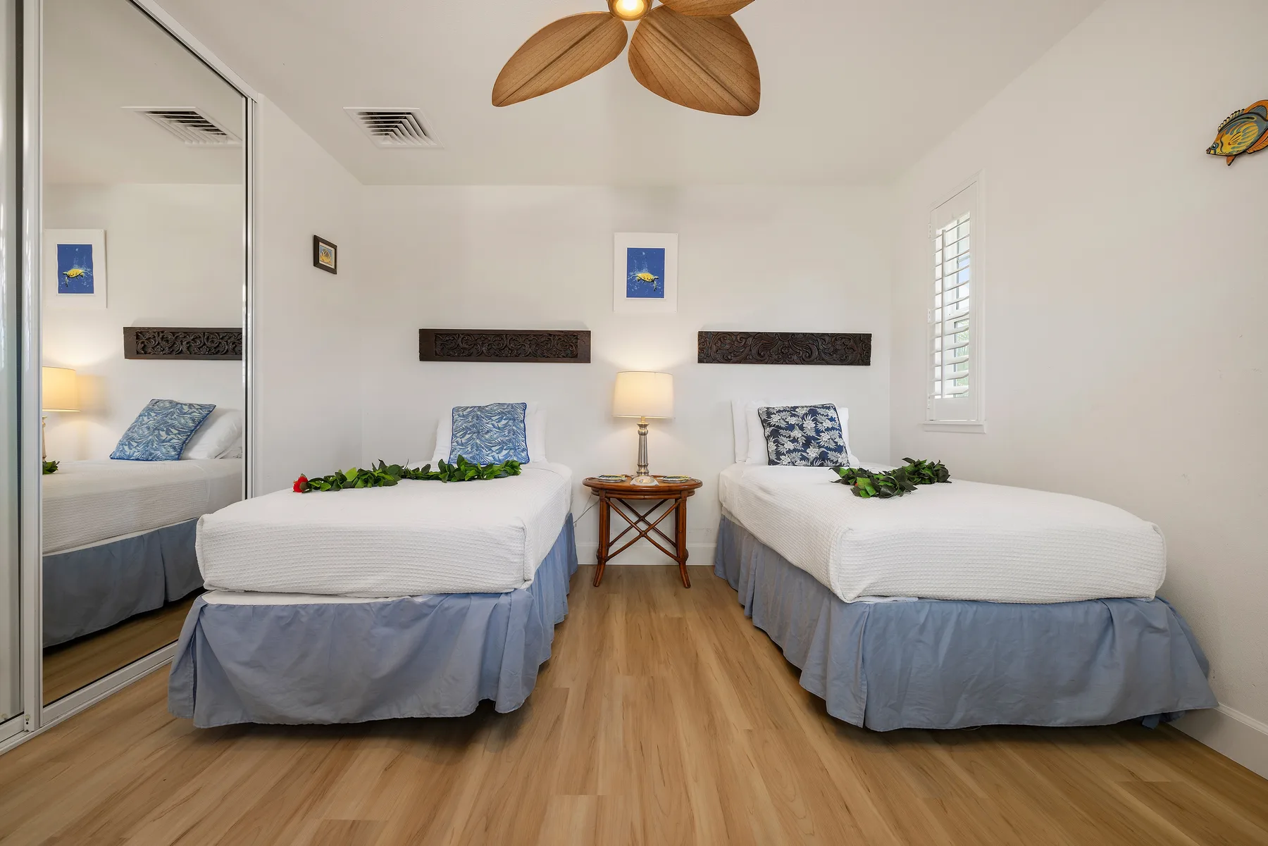 A bright bedroom with two beds, a small bedside table, and a window.
