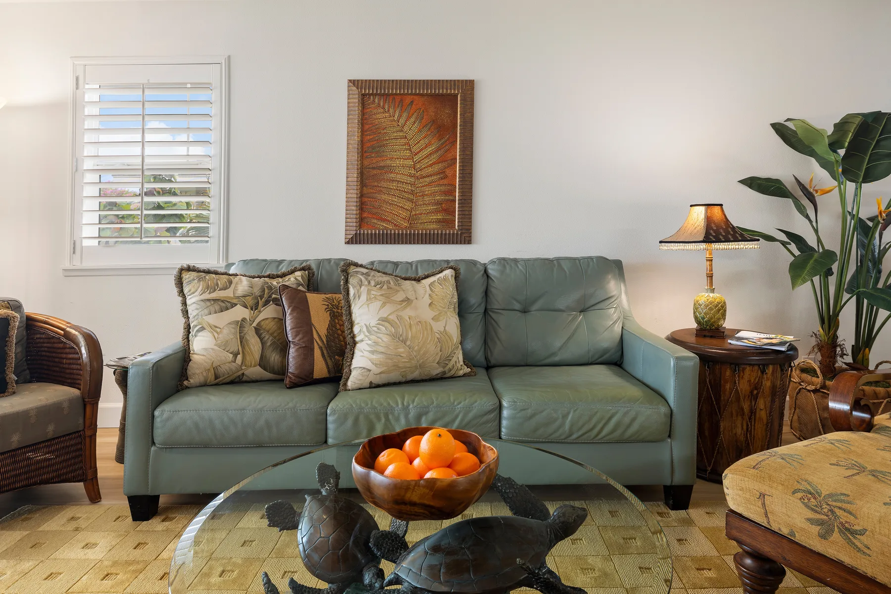 A living room with a green sofa, a glass coffee table, and a potted plant.