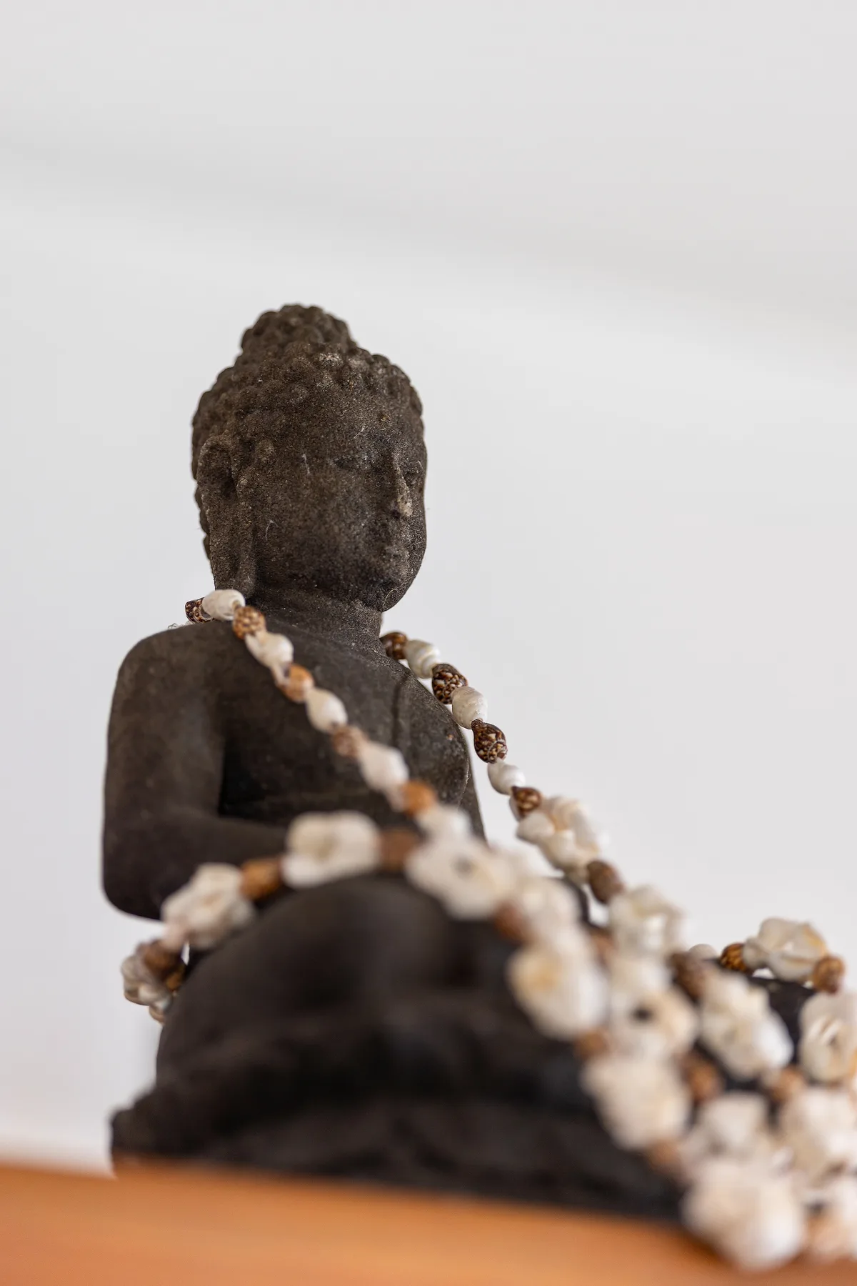 A seated Buddha statue is draped with strands of light-colored beads.