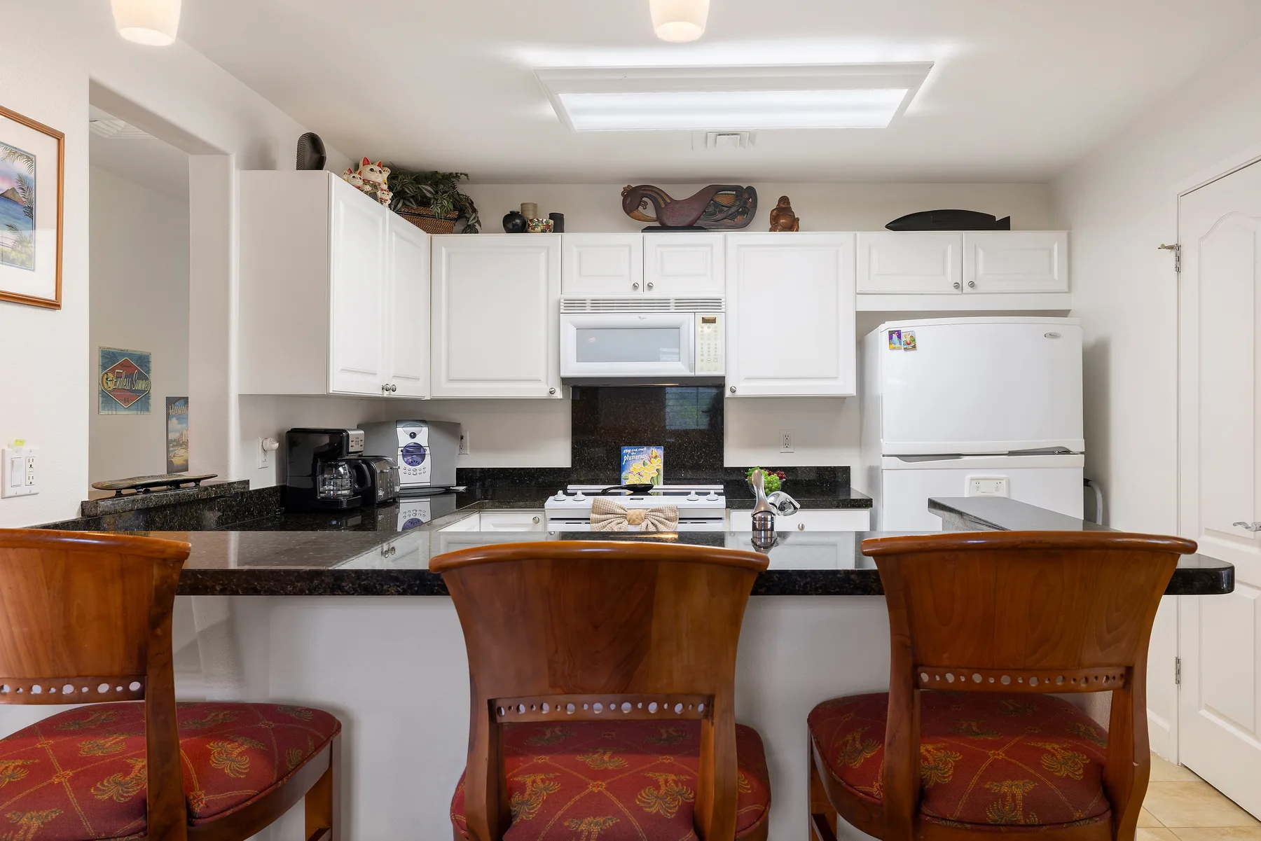 A bright kitchen with white cabinets, appliances, and a counter with seating.
