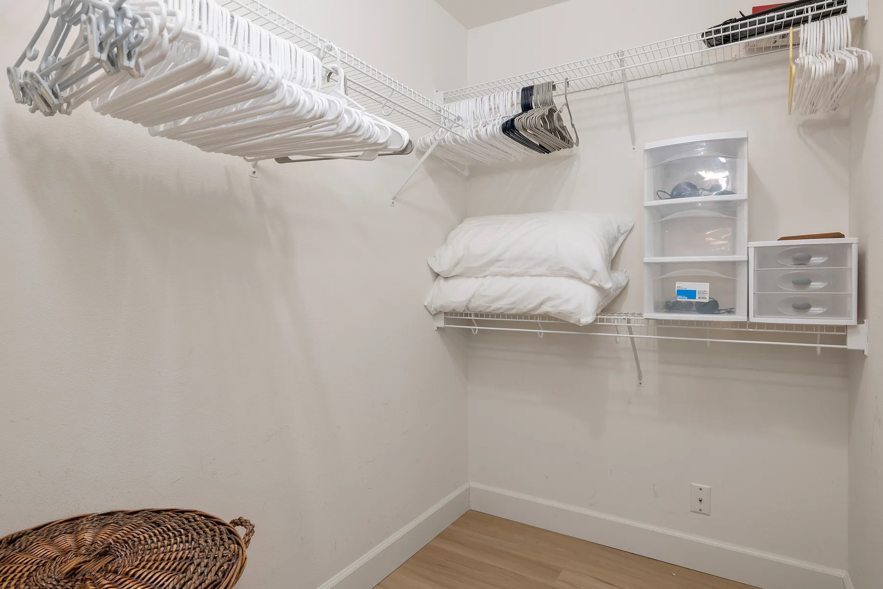 An empty walk-in closet with hanging rails, shelves, and a woven basket.