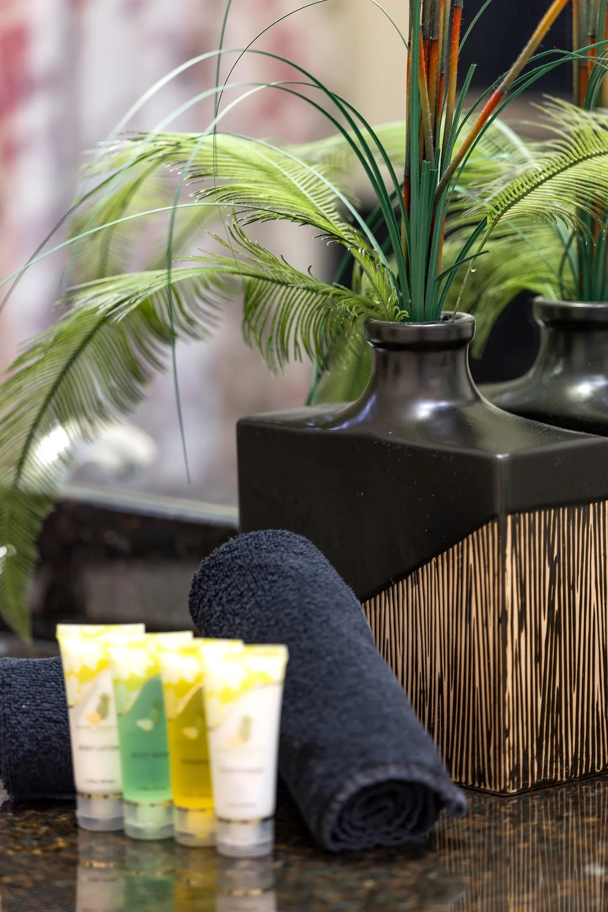 A bathroom vanity displays toiletries beside a rolled towel and a leafy arrangement.