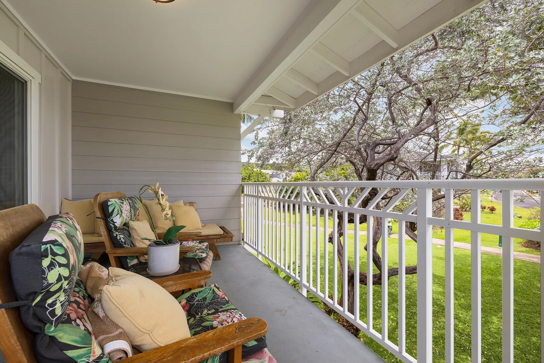 A covered porch with cushioned seating overlooks a green lawn and trees.