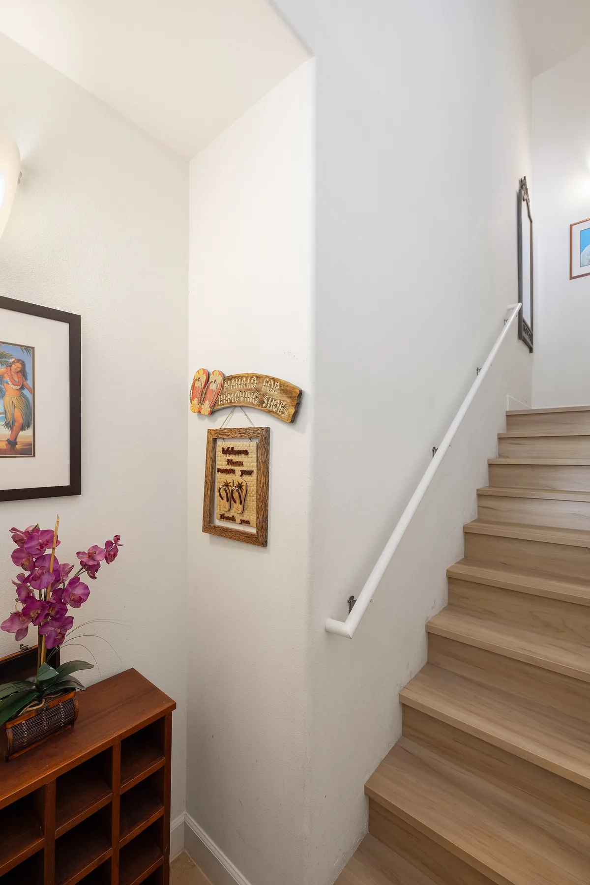 A staircase with light wood steps rises beside a white wall with framed artwork.