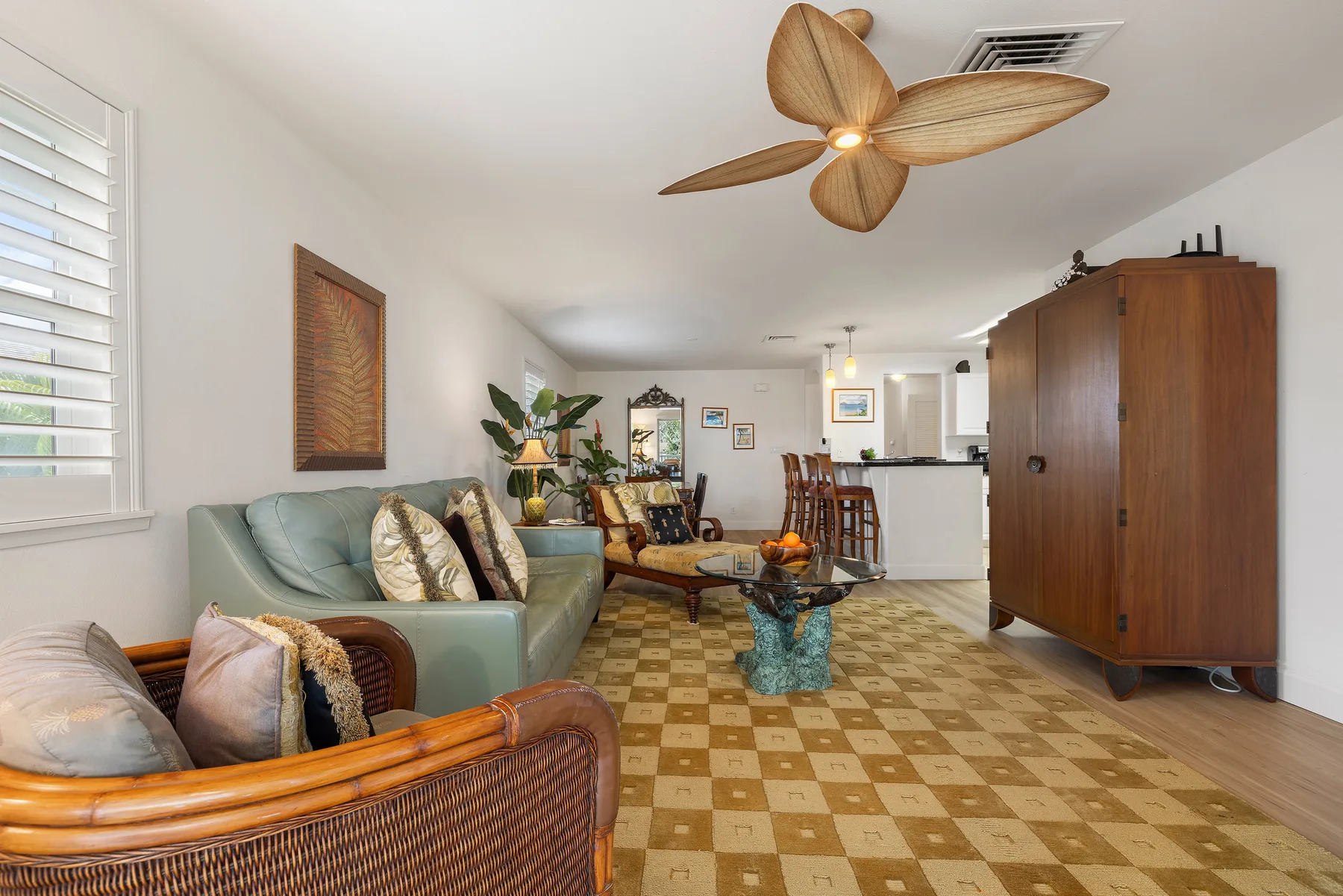 A living room with seating, a coffee table, and a kitchen beyond.
