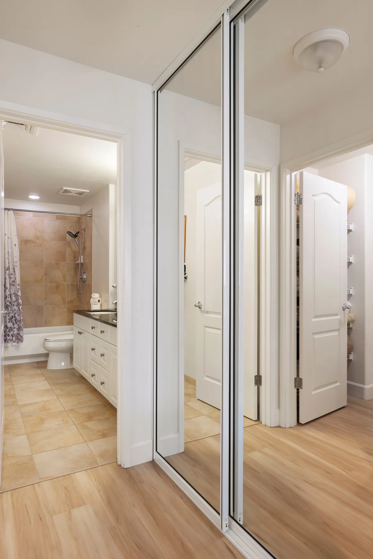 A mirrored closet door stands beside a bathroom with a bathtub and vanity.