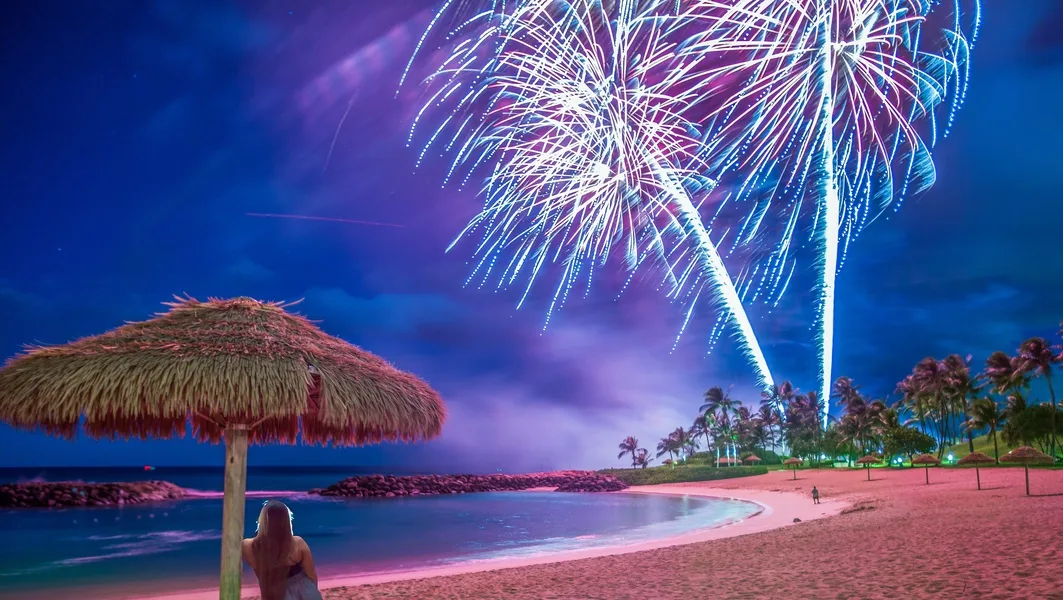A beach at night with fireworks bursting above the water.