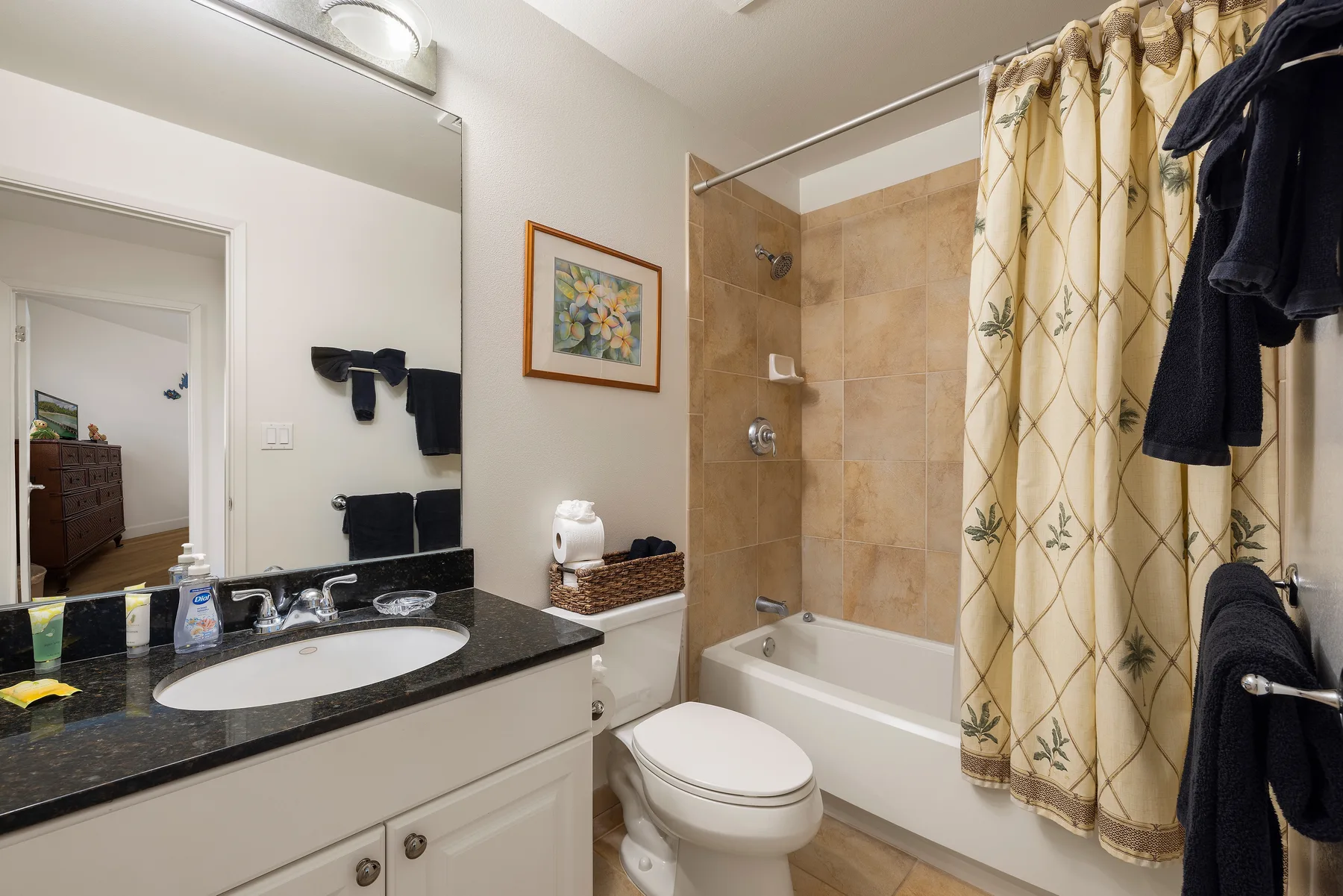 A bathroom with a vanity, toilet, and bathtub behind a patterned curtain.