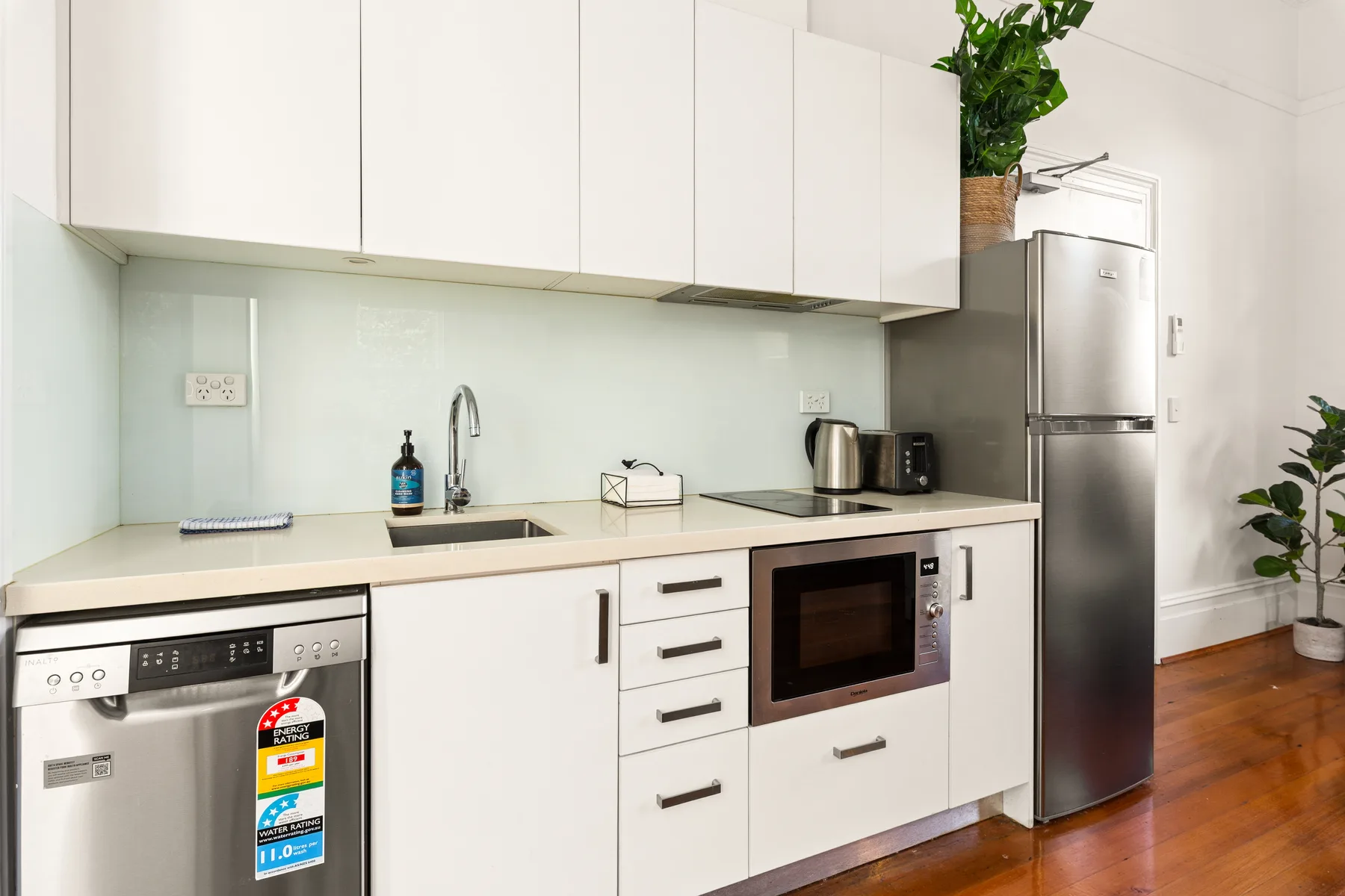 Una cocina moderna y luminosa con armarios blancos, fregadero y electrodomésticos de acero inoxidable.