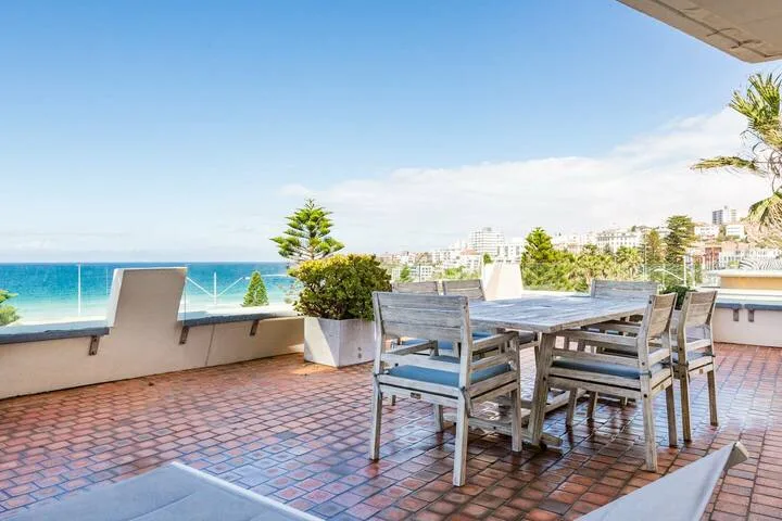 Una terraza junto al mar tiene un conjunto de comedor de madera y vistas al océano.