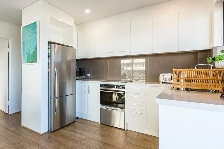 Una cocina moderna y luminosa con gabinetes blancos, electrodomésticos de acero inoxidable y suelo en tono madera.