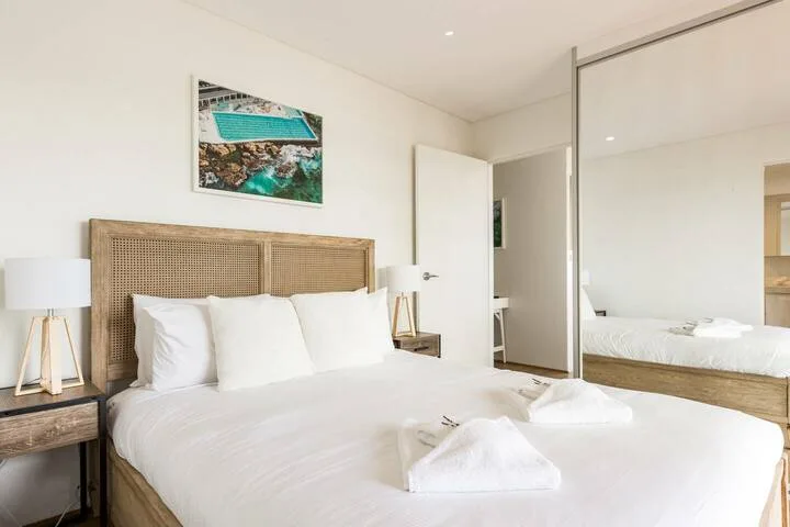 Un dormitorio luminoso con una cama bien tendida y un cabecero tejido.