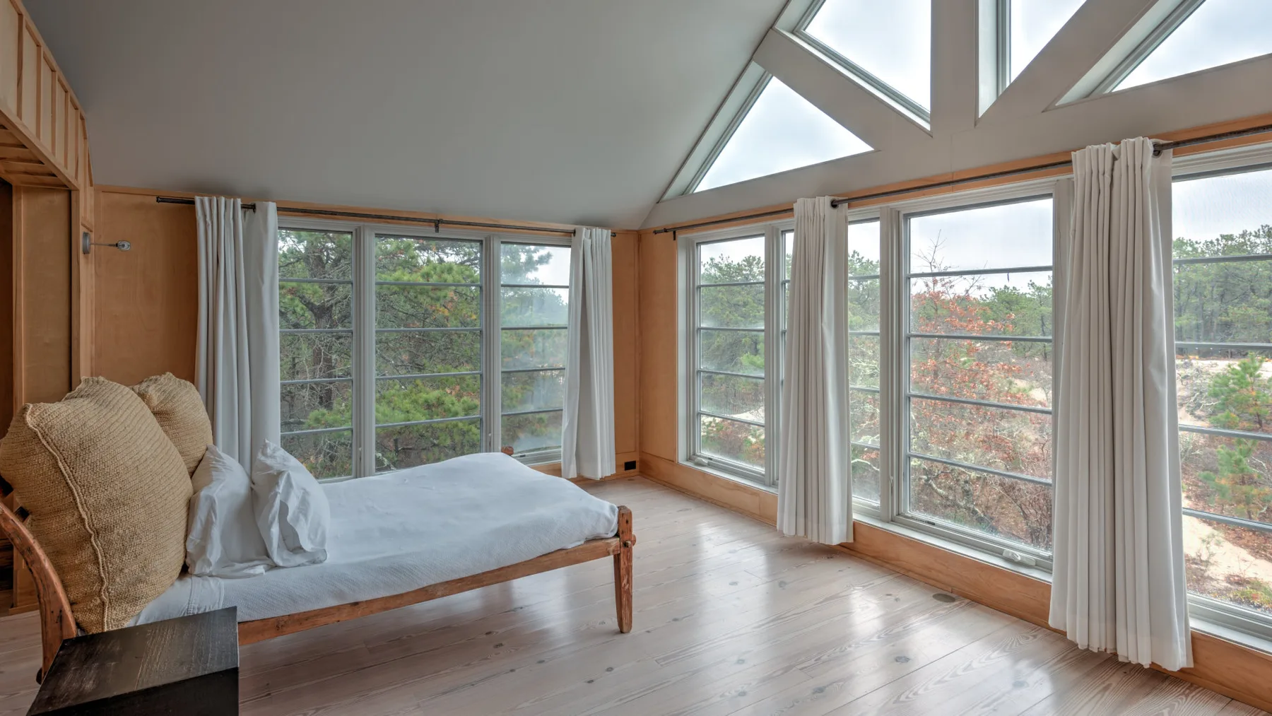 Un dormitorio luminoso con una cama de madera junto a grandes ventanas.