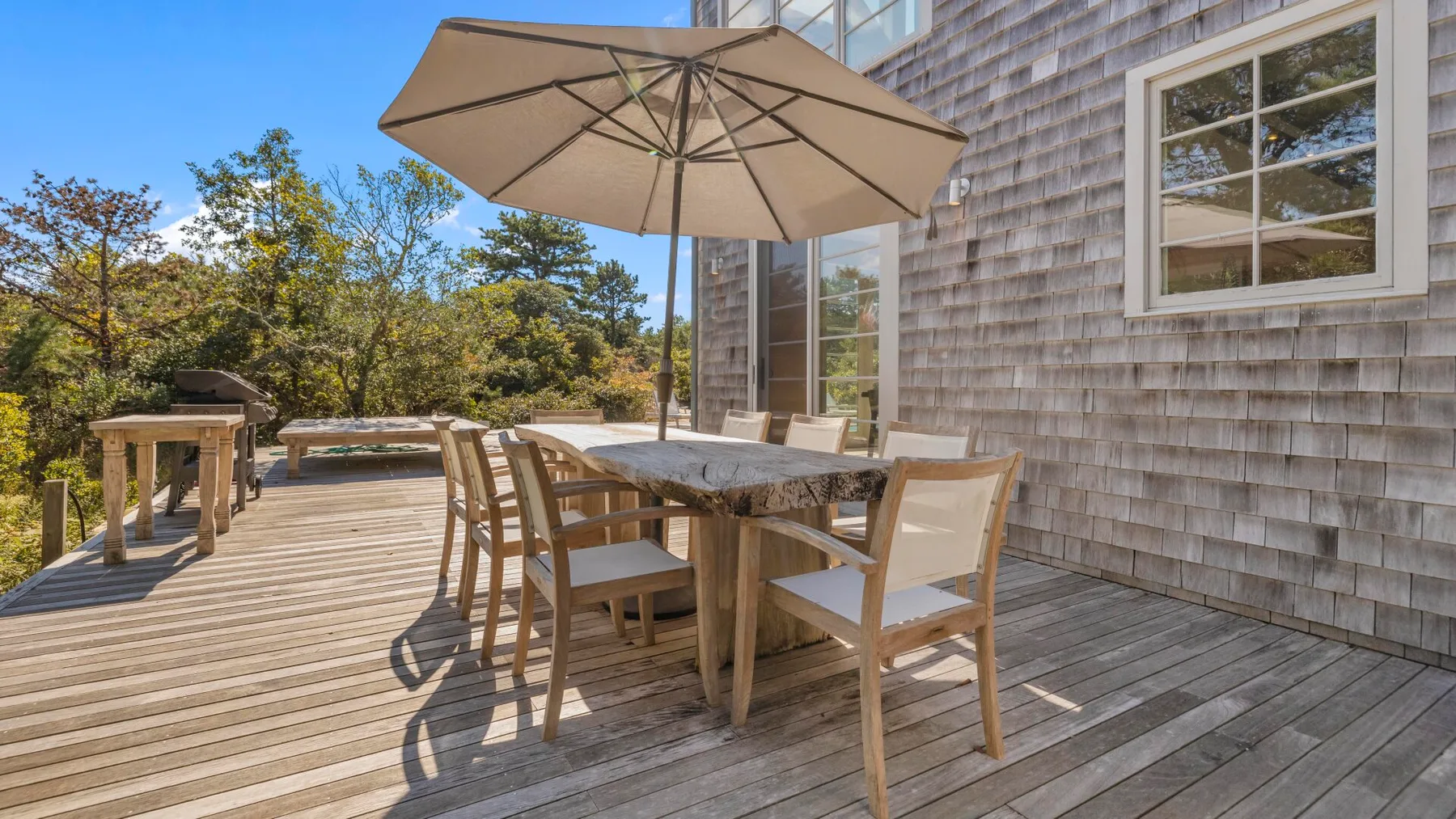 Una terraza exterior tiene una mesa de comedor y asientos bajo una sombrilla grande.