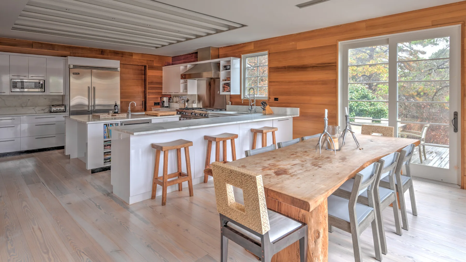 Una cocina luminosa con comedor y una mesa larga de madera junto a puertas de vidrio.