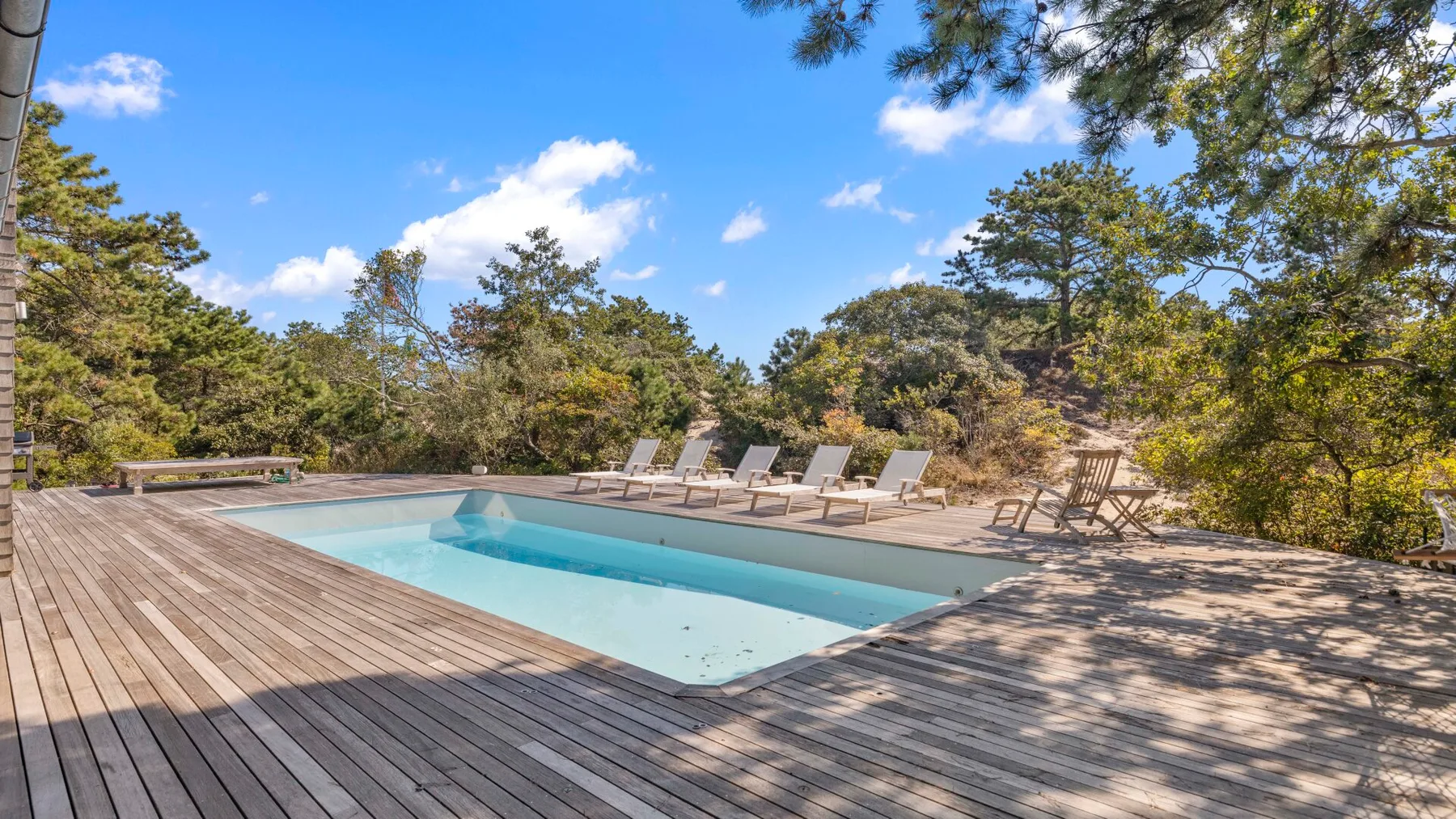 Una piscina al aire libre está rodeada por una terraza de madera y árboles.