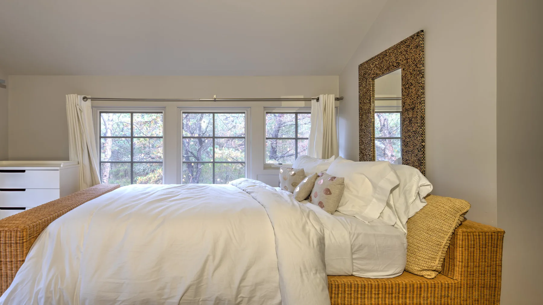 Un dormitorio con una cama, ropa de cama blanca y ventanas grandes.