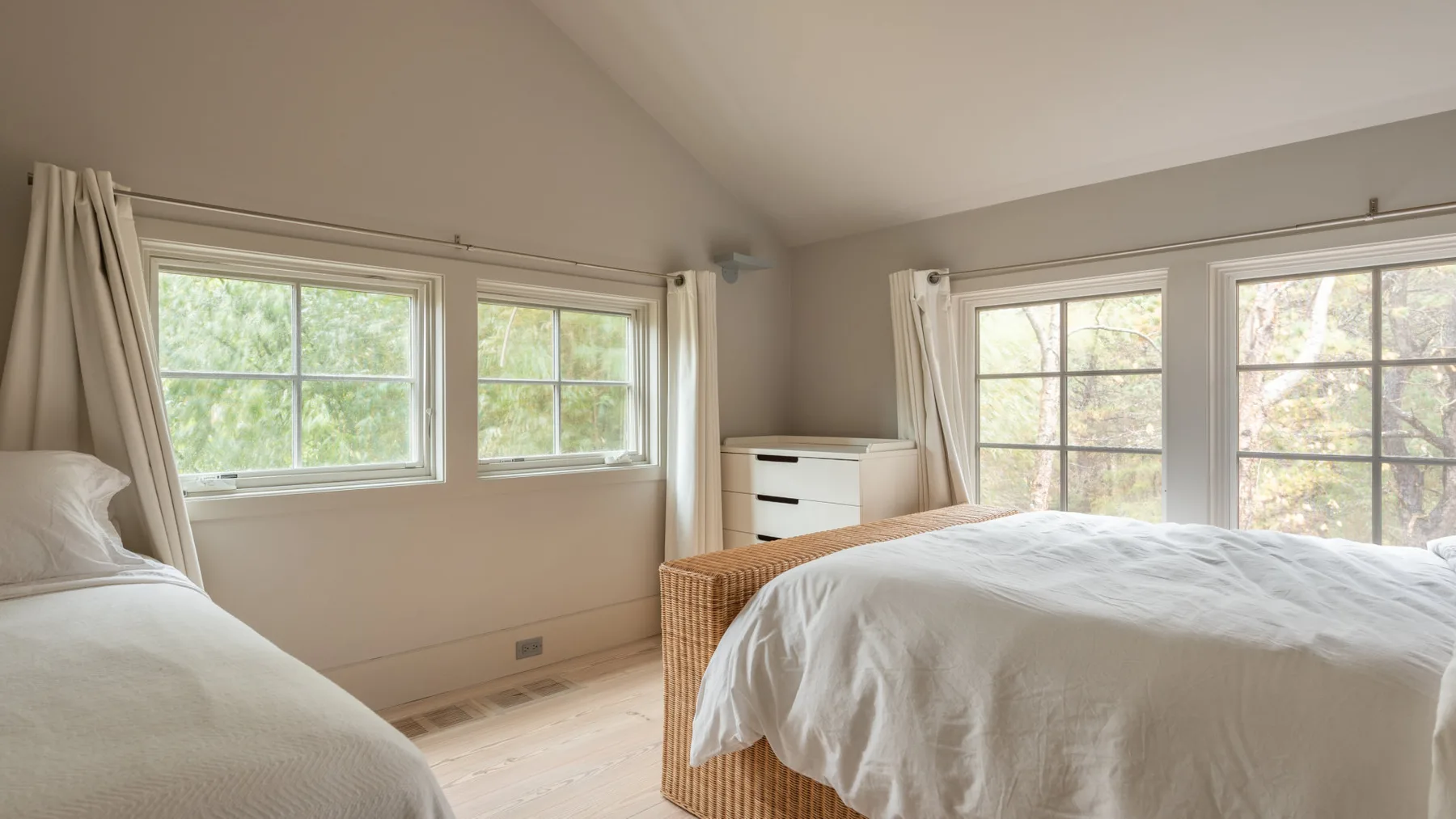 Un dormitorio luminoso con camas junto a grandes ventanas y cortinas claras.
