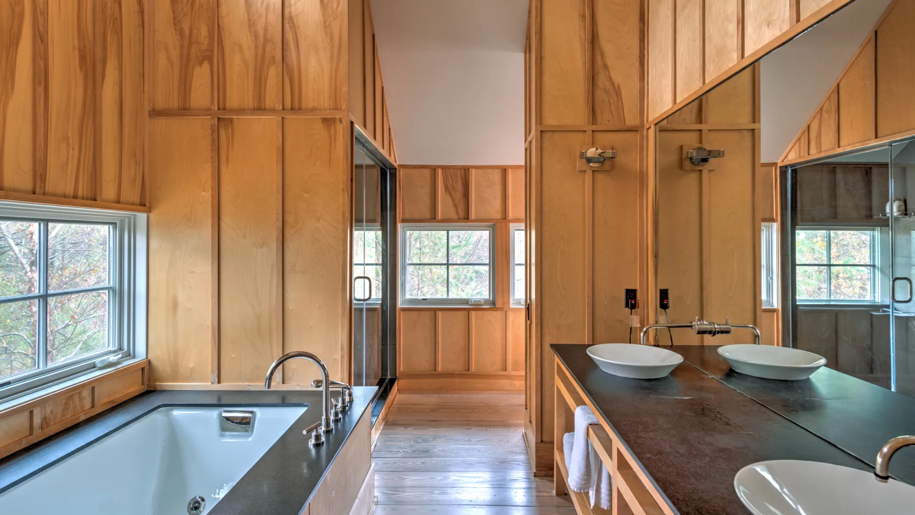Un baño revestido de madera con bañera, encimera y lavabos sobrepuestos.