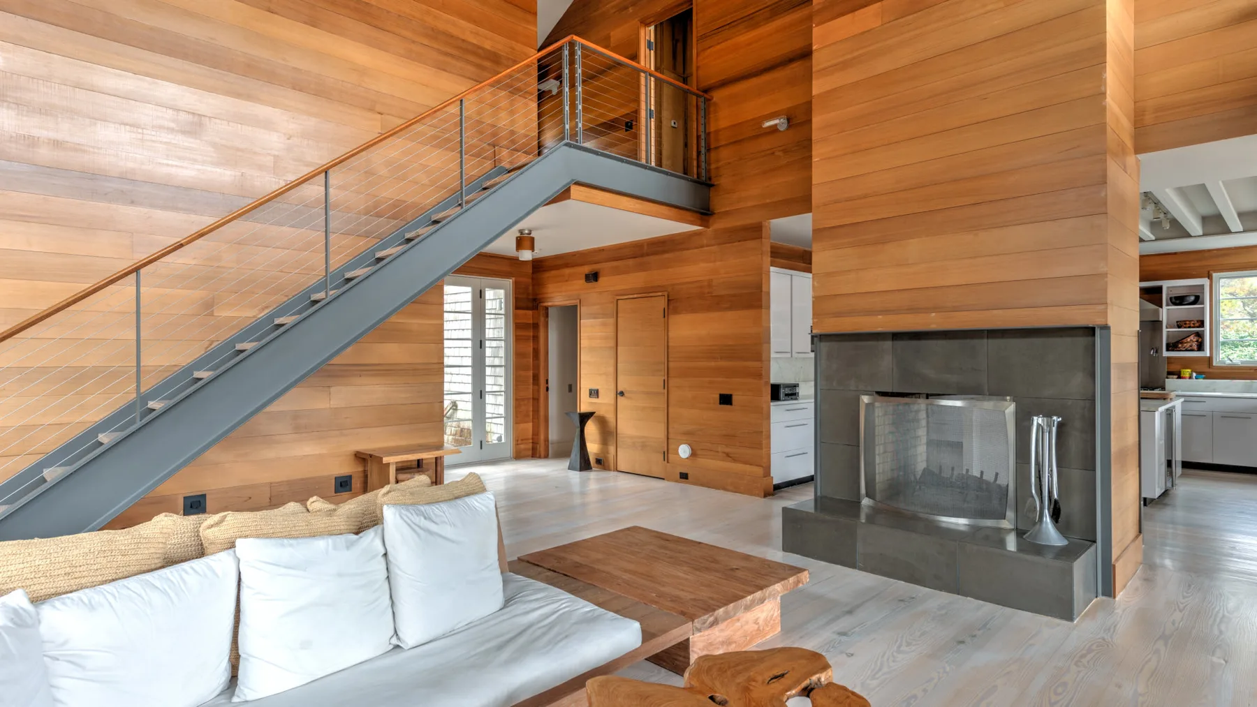 Una sala revestida de madera tiene una escalera y una chimenea junto a la zona de asientos.