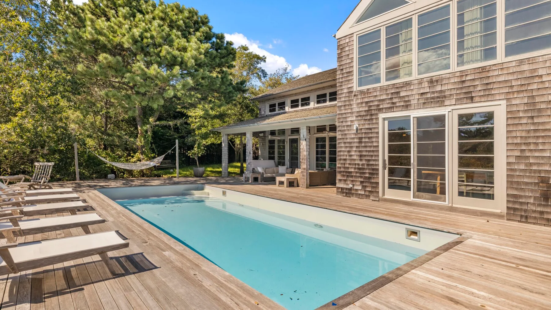 Una piscina está junto a una terraza de madera y una casa grande.