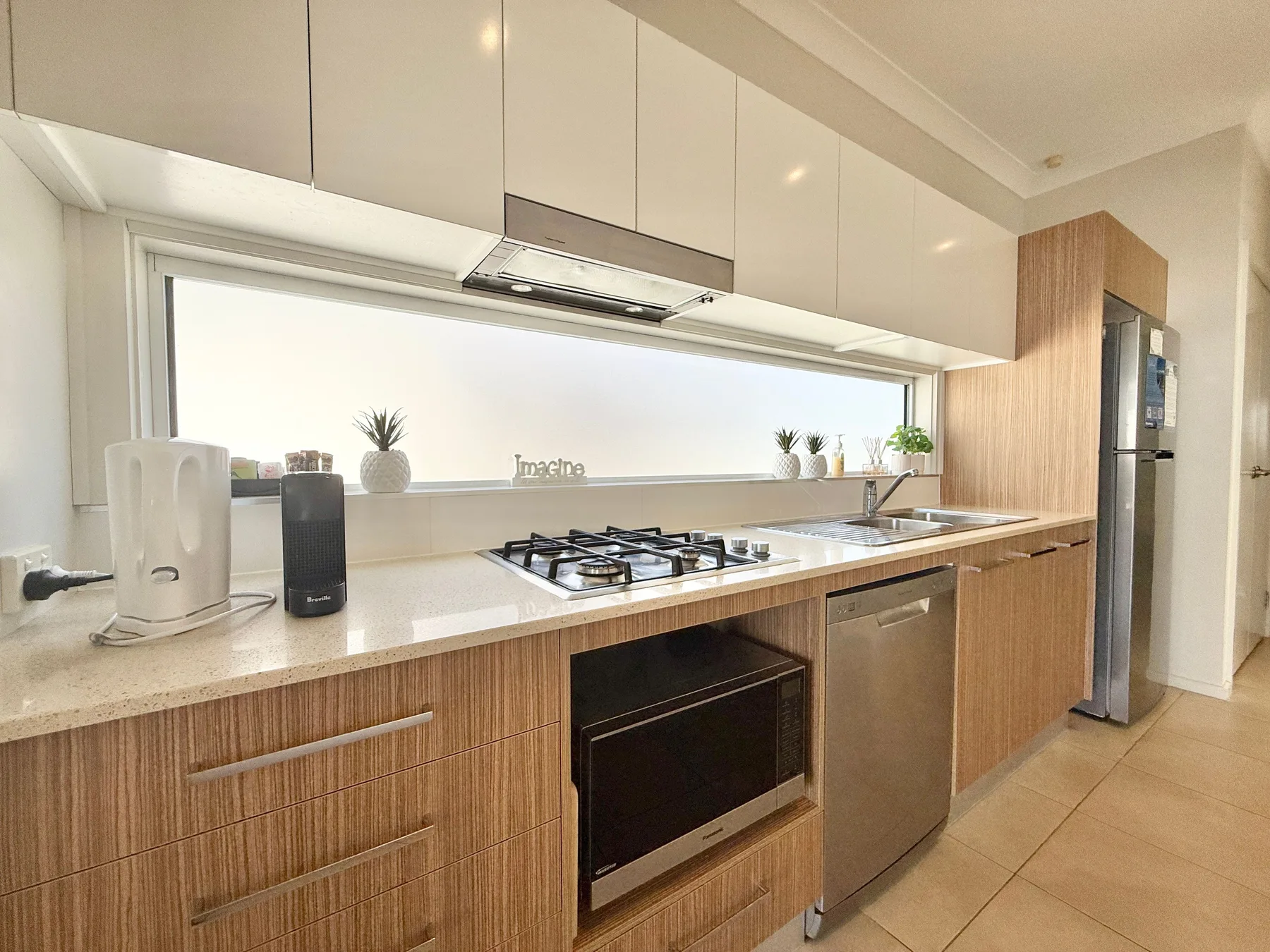 A bright modern kitchen with a cooktop, oven, and stainless-steel appliances.